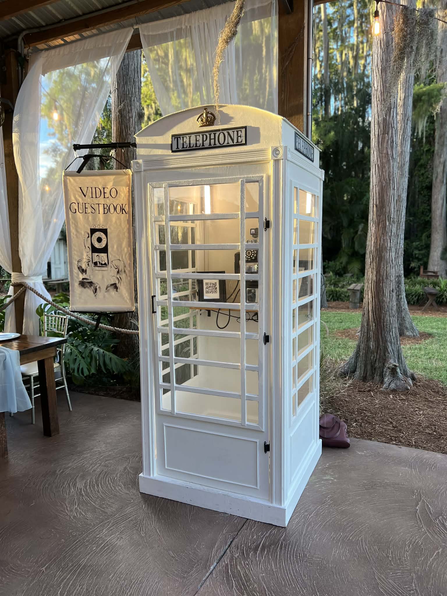 White vintage telephone booth with rotary phone and open door at an outdoor wedding